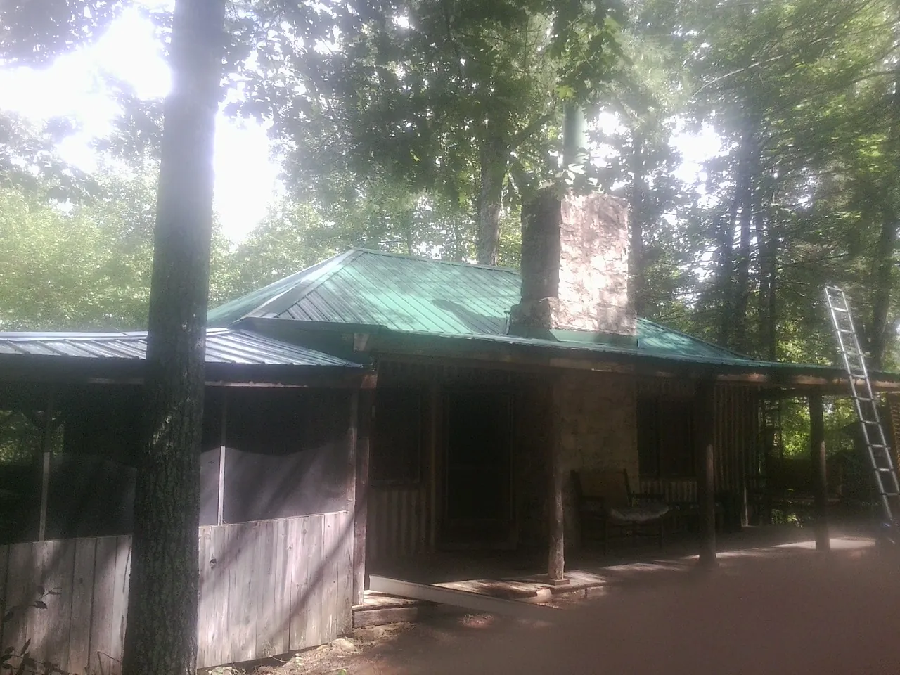Green metal roof and stone chimney above a log cabin porch in Byron